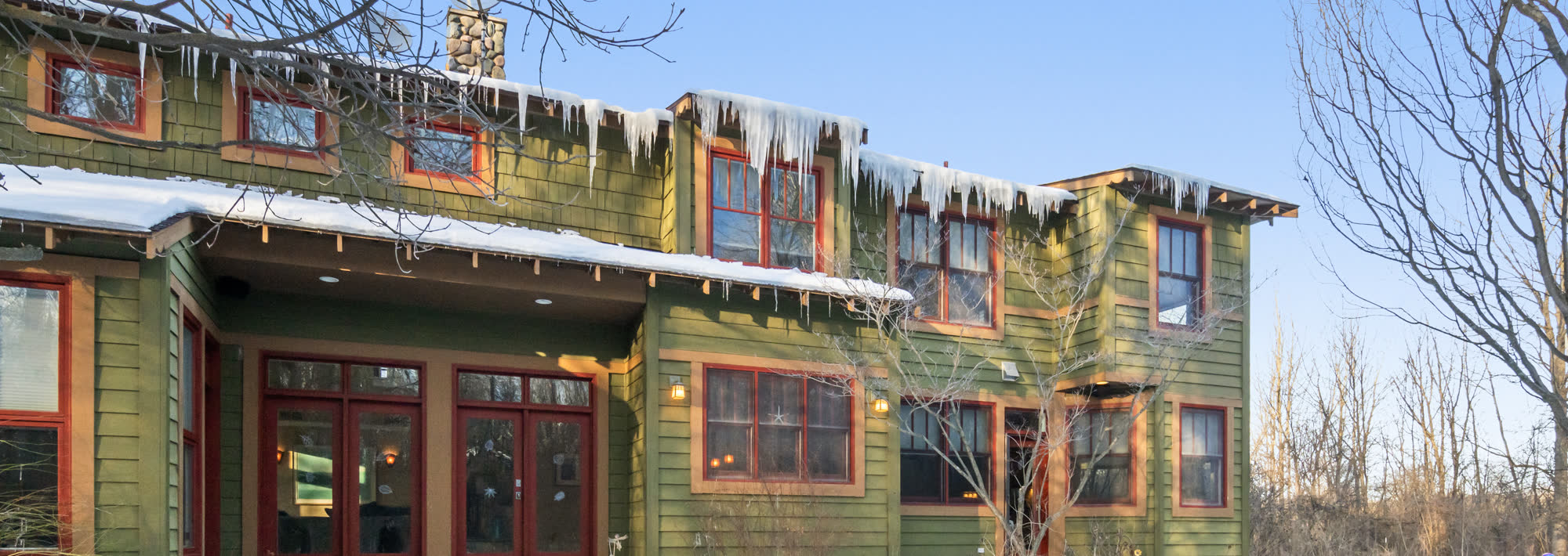 Icicles along the roofline of a green craftsman home in winter