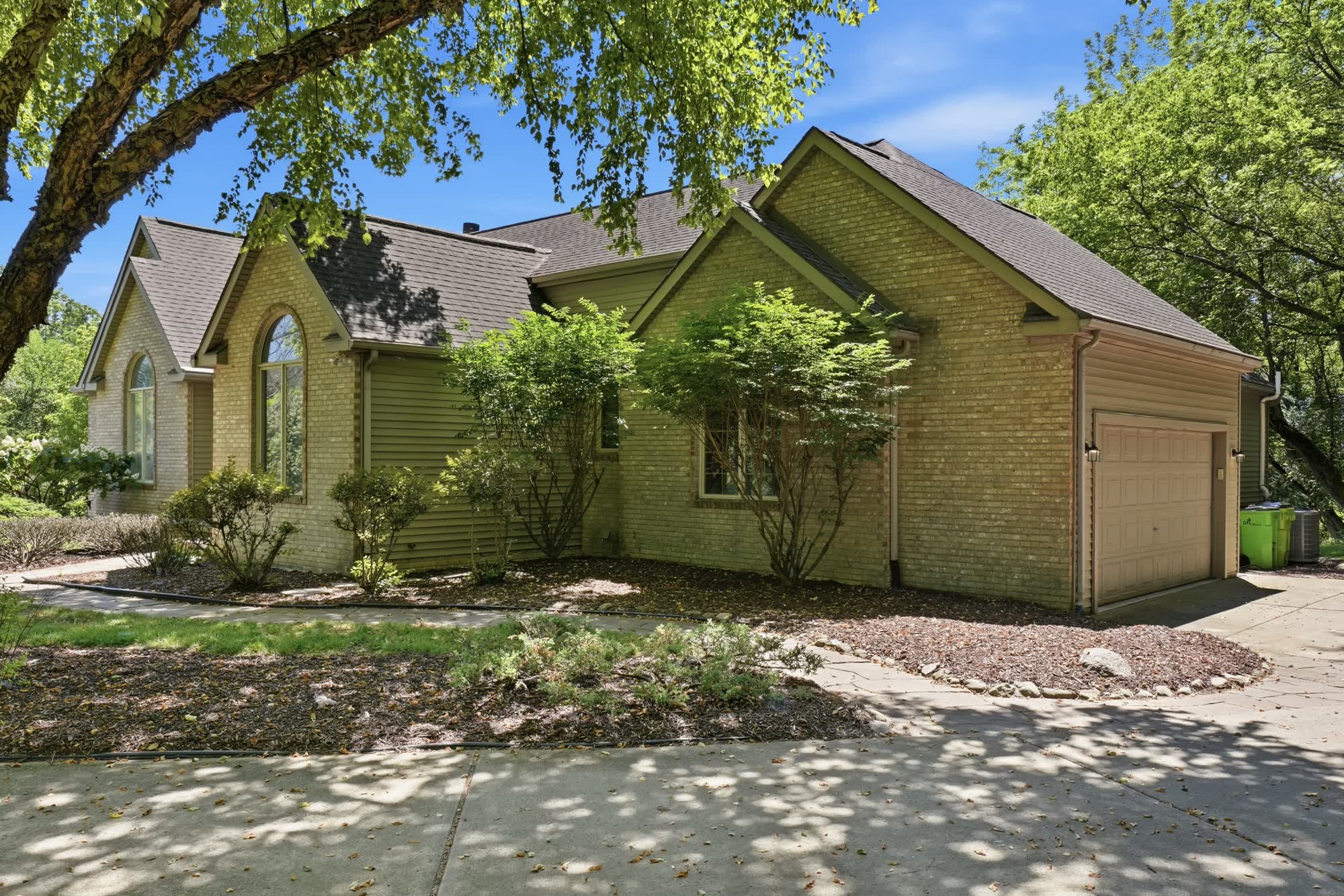 The same home photographed again in summer 2026, with green trees and a blue sky