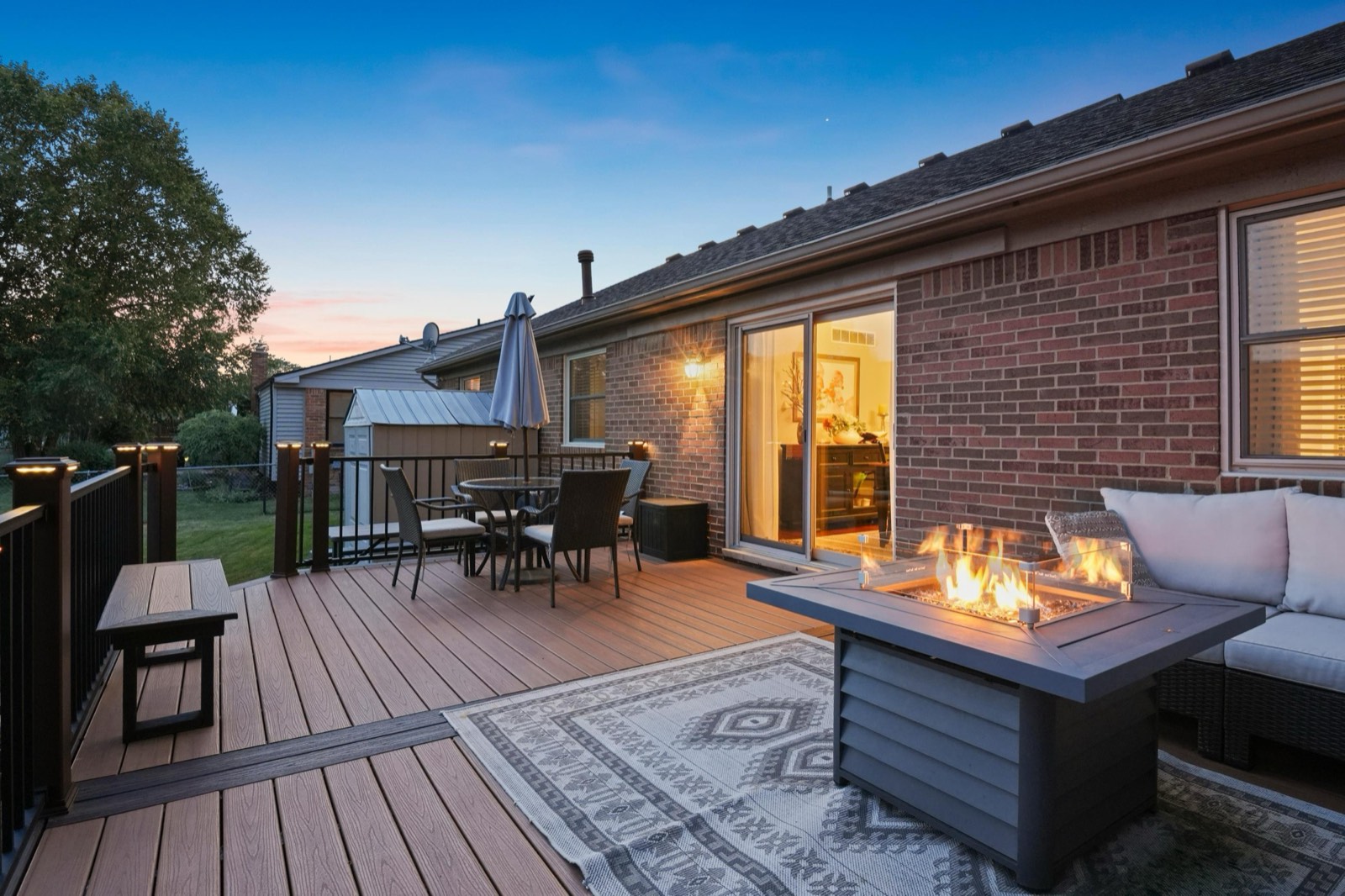 Deck photographed at dusk with the fire table lit and the house glowing behind it